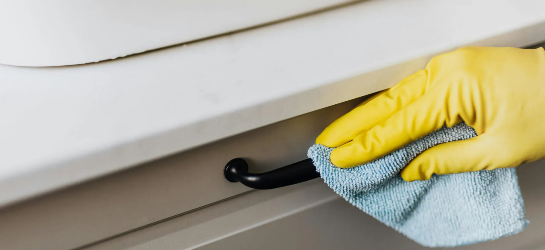 Gloved hand wiping a kitchen cabinet handle during kitchen cleaning